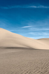 Deserted landscape. Sand dune with dark shadow on a background of blue sky.