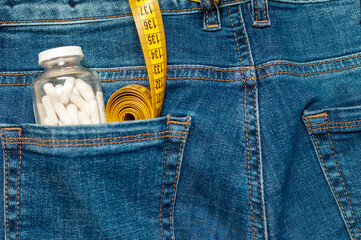 yellow measuring tape and a glass jar with pills are in the back pocket of blue jeans.