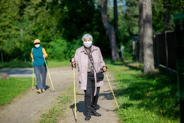 Senior women wearing medical masks walking with nordic walking poles during covid-19 pandemic