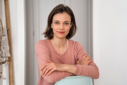 Smiling woman with arms crossed sitting on chair at home