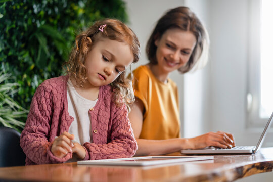 Daughter using tablet PC by smiling mother working at home office