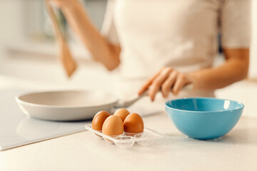 Obraz na płótnie Canvas Close of organic eggs om kitchen counter with woman in blurry background making a breakfast.