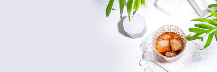 Strong alcohol drink glass. One glass of cognac or whiskey with ice cubes on white tile background with summer sunlight copy space