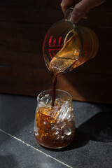 Ice coffee on a black table with cream being poured into it showing the texture and refreshing look of the drink