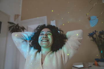 Happy woman with hands behind head and eyes closed sitting under astro lights at home