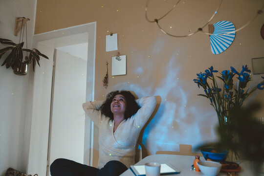 Smiling woman with hands behind head looking at astro light effects in room