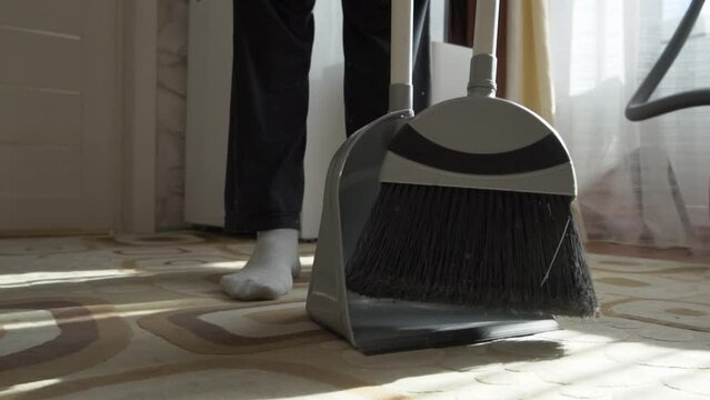 Sweep the dust from the floor with a brush. Dust rises into the air.  Sweep the dirt from the carpet in a dustpan. Clean the house. Do the cleaning. Close-up.  Cleaning service. Home cleaning routine.
