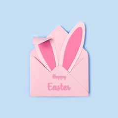 Happy Easter. Bunny rabbit ears made of pink paper in pink envelope on blue background. Easter greeting card with envelope. Happy Easter minimal concept with copy space. Square format, Flat lay