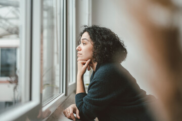 Thoughtful woman looking through window at home