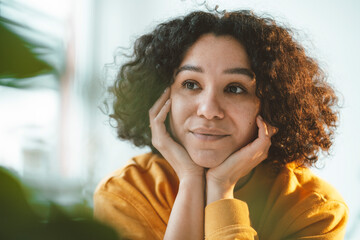 Thoughtful woman with curly hair sitting with head in hands at home