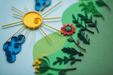 Selective focus of composition of paper sun with clouds with flowers and leaves isolated on a green and blue paper background. Hand made of paper quilling technique.