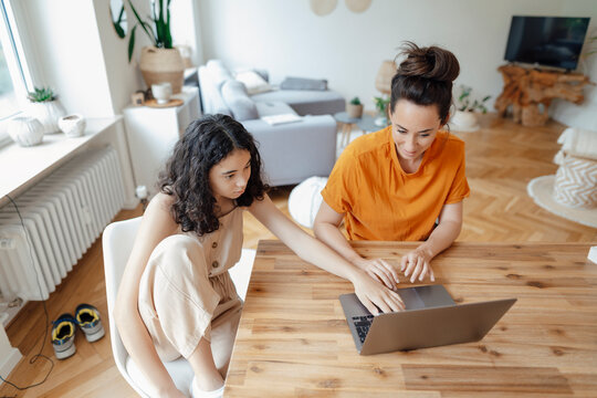 Teenage girl using laptop with mother at home