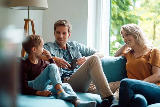 Son talking with mother and father sitting on sofa in living room