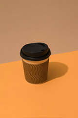 Brown eco coffee cup with black plastic lid on orange and brown background with copy space. Vertical composition