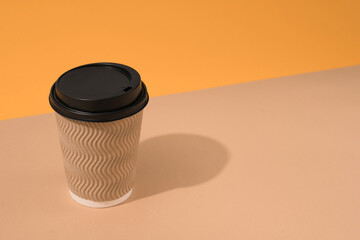 Mockup image of brown kraft paper coffee cup with plastic lid on orange and brown background with copy space. Sustainable food packaging concept