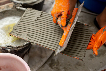 Builder tiling a concrete wall with decorative ornamental tiles lining up a tile with his gloved hands to seat into the tiling cement on the wall.
