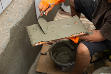 Builder tiling a concrete wall with decorative ornamental tiles lining up a tile with his gloved...