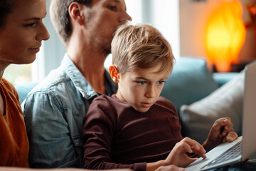 Blond boy using laptop sitting with parents at home