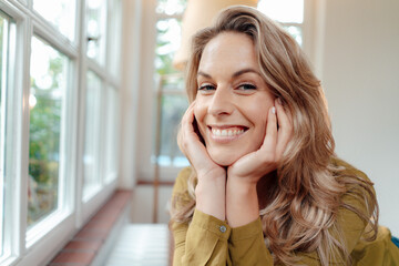 Happy beautiful blond woman with head in hands at home