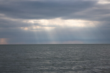 Obraz premium Calm seascape with stormy sky where sun-rays get through the clouds.