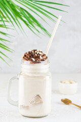 Coconut milkshake with chocolate and nuts on the background of a palm branch. Vegan, sugar and lactose free.