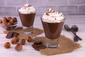 Chocolate mousse with hazelnuts and cream on a white wooden background.