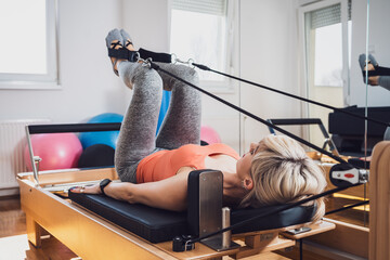 Woman is exercising on pilates reformer bed at home.