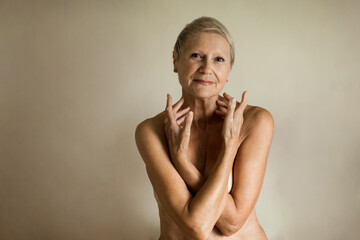 Smiling topless senior woman covering breasts against white background