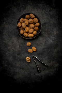 Studio shot of nutcracker and bowl of walnuts lying against black background