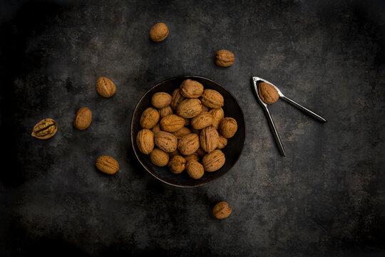 Studio shot of nutcracker and bowl of walnuts lying against black background