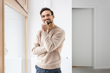 Smiling man with hand on chin standing near window at home