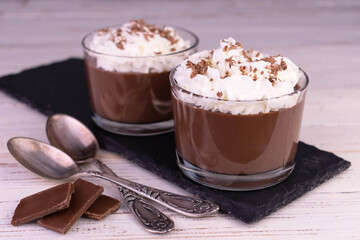 Chocolate pudding with whipped cream in glasses on a black slate board.