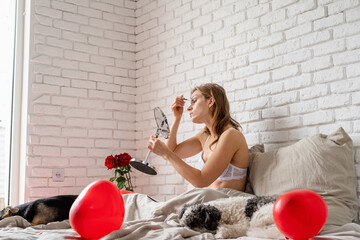 Woman sitting on bed with her funny dog at home and applying cosmetics