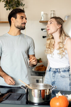 Couple slurping noodle standing in kitchen at home