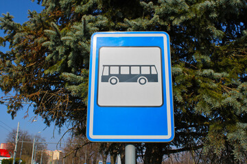Bus station traffic sign with tree in the background. The sign consists of black bus in the white...