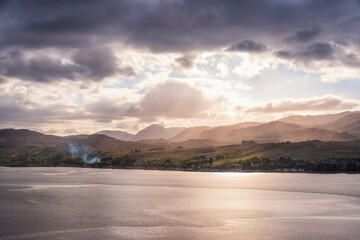 Scenic view of sea with mountains in background under cloudy sky on sunset