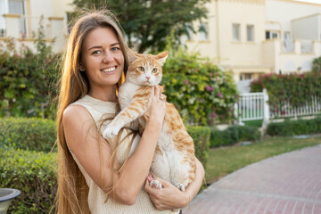 Happy woman with long blond hair holding ginger cat in garden