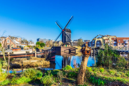 Netherlands, South Holland, Leiden, Clear blue sky over city canal with traditional windmill in background