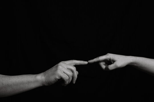 Black and white image of two hands that are joined in the center by one finger. Hand of man and woman generating connection by the contact of a finger.
