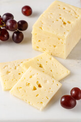 Cutting a piece of aromatic cheese  and red grapes on marble board in the kitchen.