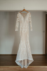 Wedding dress hangs on a chandelier in a white room.