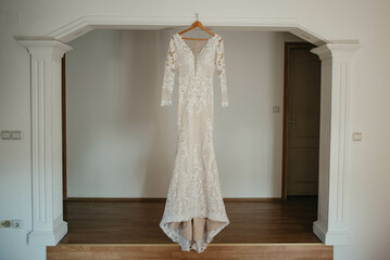 Wedding dress hangs on a chandelier in a white room.