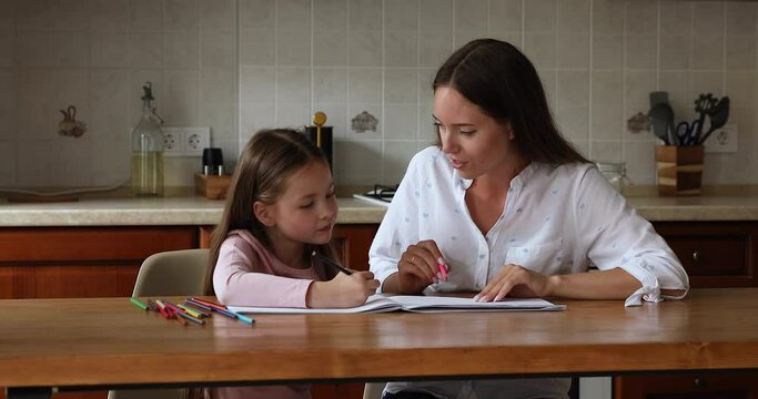 Young loving mother and little pretty daughter draw with colored pencils seated at table in cozy domestic kitchen, caring parent develop skills of child, children growth, common hobby at home concept