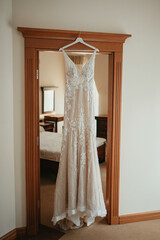 Wedding dress hangs on a chandelier in a white room.