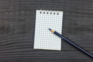 Notepad (notebook) and pencil on black wood background (copy space).