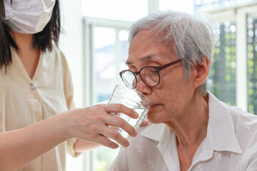 Nurse or caregiver gives water to senior woman,taking care,feeding water,thirsty asian old elderly drinking fresh water to quench their thirst in hot summer weather,preventing dehydration,health care