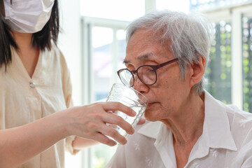 Nurse or caregiver gives water to senior woman,taking care,feeding water,thirsty asian old elderly...