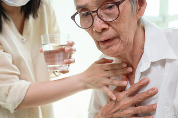 Asian senior woman coughing choking while drinking water or eating food,danger or risk of lung infection,disease of silent aspiration pneumonia,old elderly patient choking water after taking the pills - obrazy, fototapety, plakaty