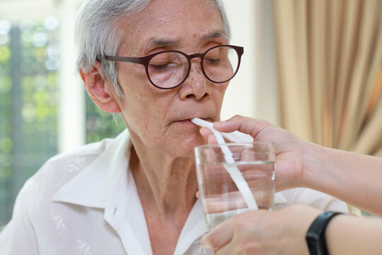 Nurse or caregiver taking care of disabled senior grandmother gives drinking water,feeding water using a straw to prevent choking and  difficulty or discomfort in swallowing,dysphagia in the elderly