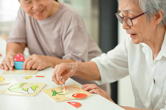 Happy asian senior woman holding picture puzzle pieces,old elderly playing a jigsaw puzzle at home,training memory and brain development,practice hands or fingers muscle exercise in picking up objects